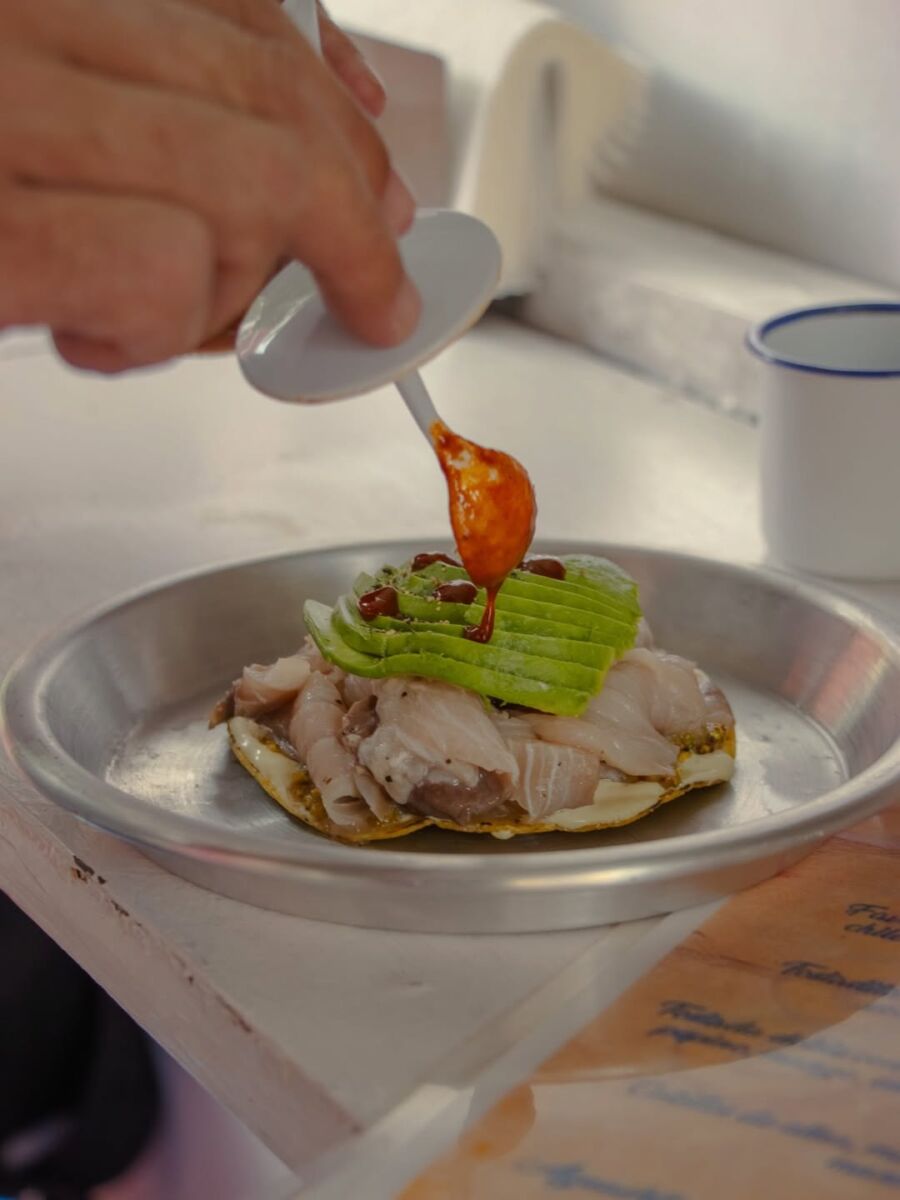 persona echando salsa a una tostada de pescado 