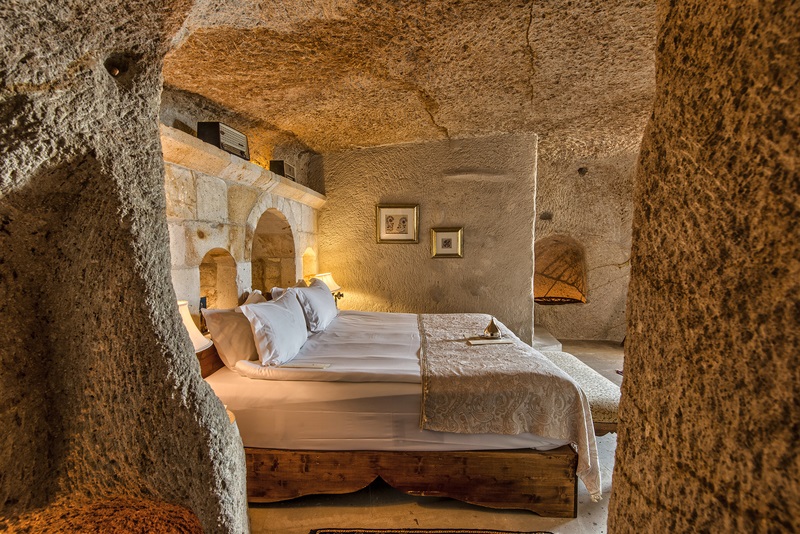 habitción con muros de piedra blanco y cama lujosa con textiles blancos
