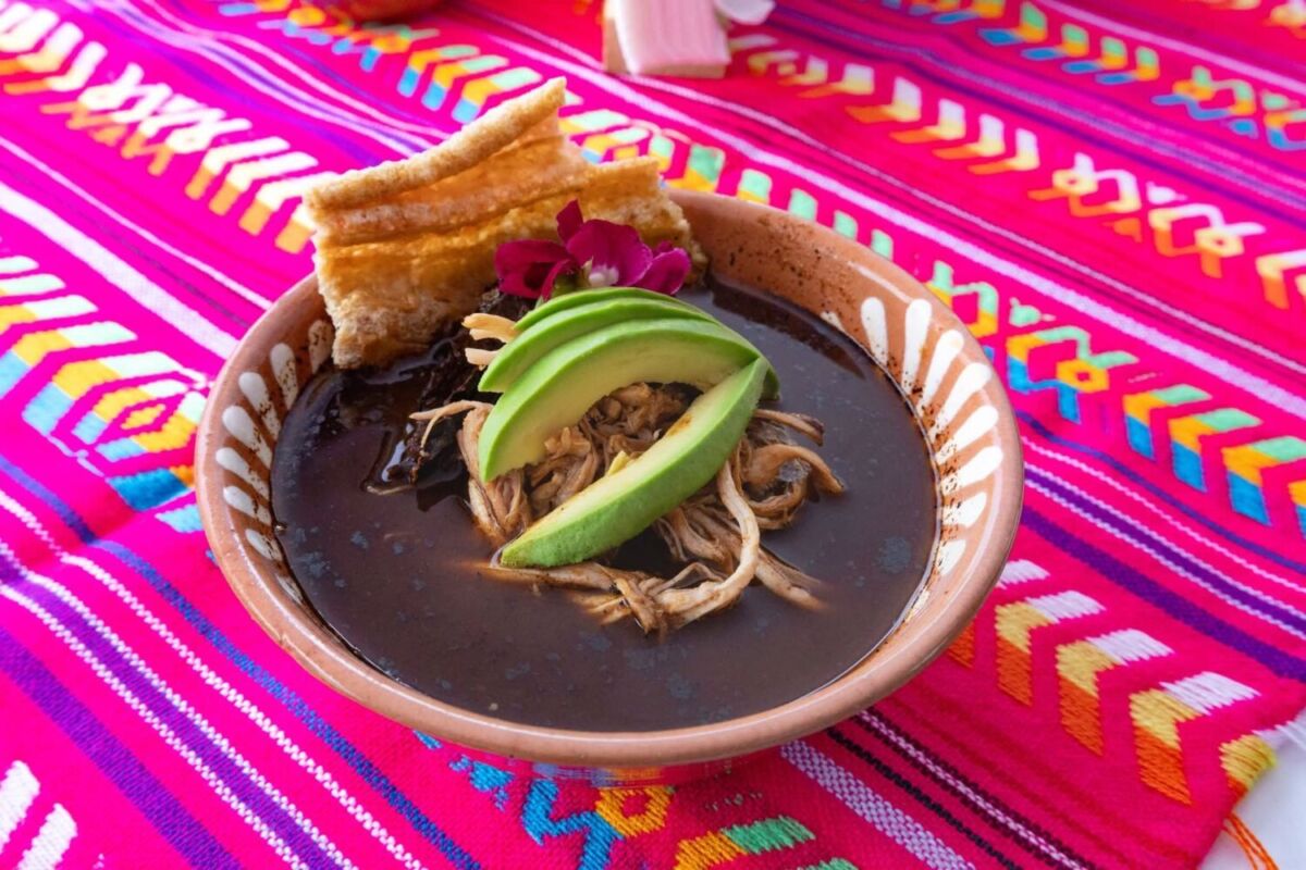 plato de pozole negro en un mantel rosa con colores