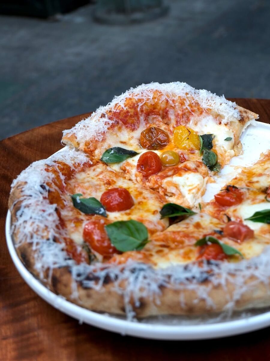 pizza napolitana con queso en las orillas, jitomate cherry y albahaca