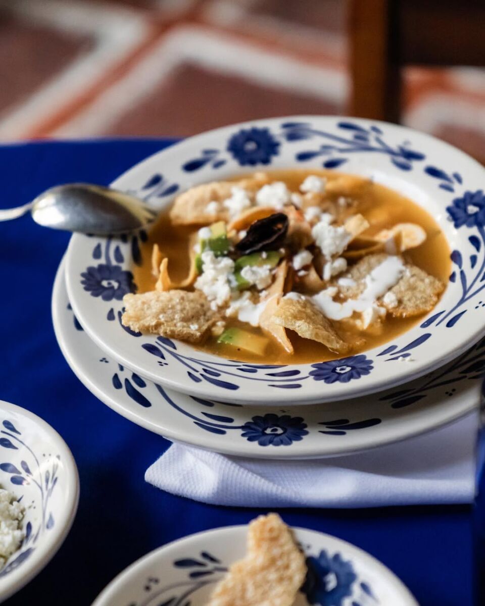 sopa mexicana preparada con tortilla, chicharrón, crema, queso y aguacate 