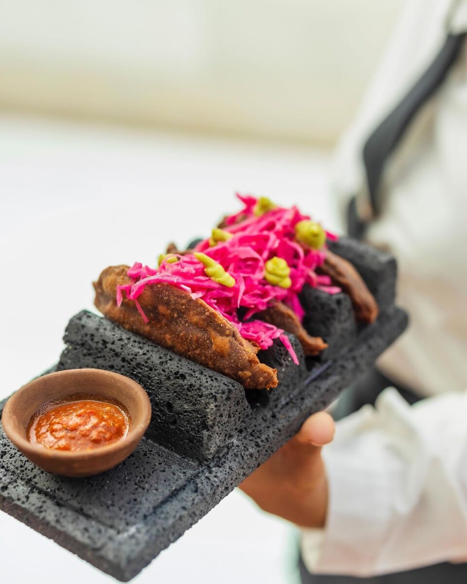 tacos fritos con cebolla morada en un plato de piedra volcánica
