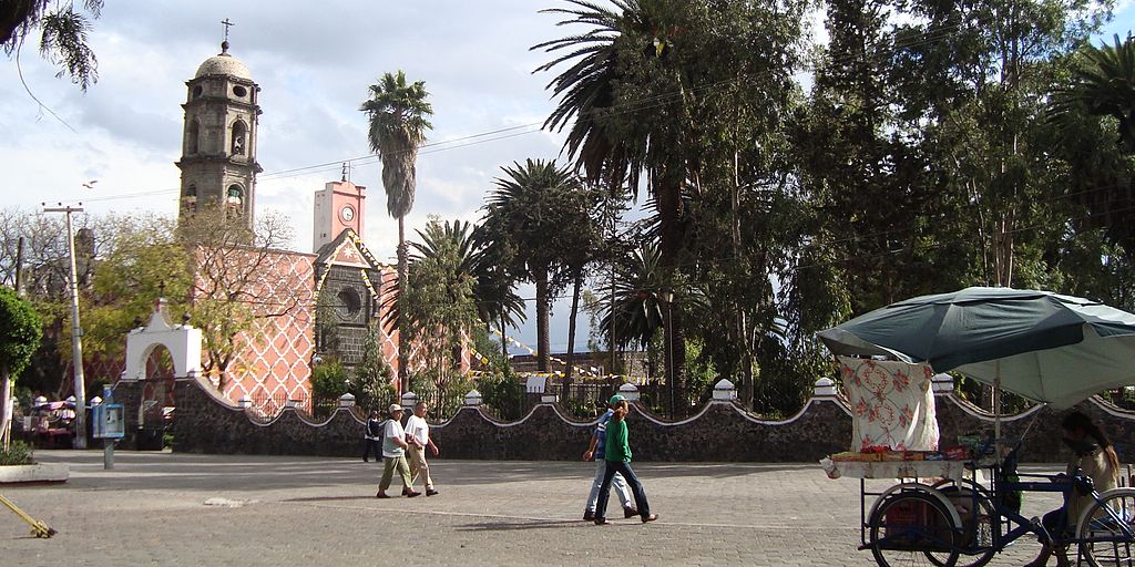 plaza mexicana con gente caminando y con una iglesia y palmeras al fondo