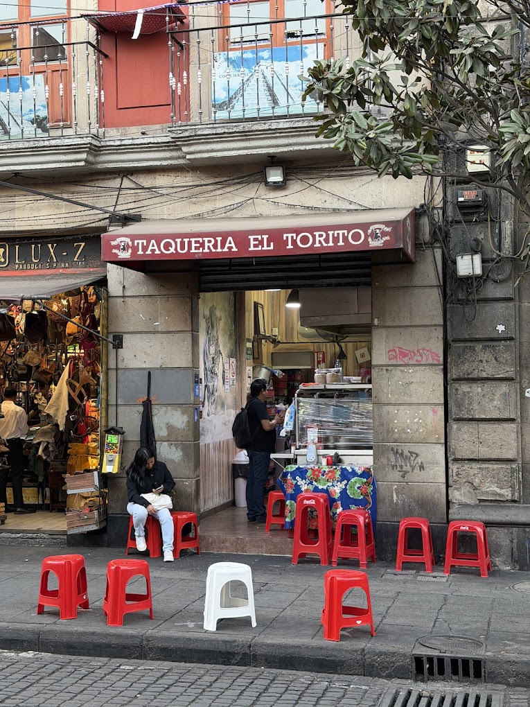 pequeño local de tacos con bancos en la banqueta