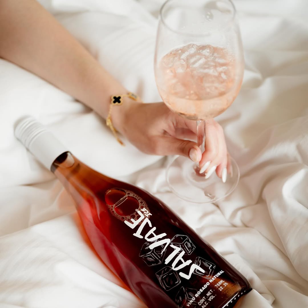 mujer sosteniendo una copa de vino con hielo junto a una botella de vino rosado salvaje