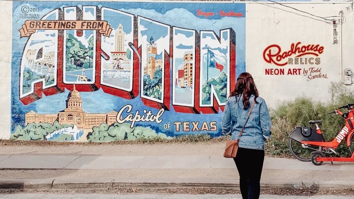 mujer de espaldas frente al mural greetings from austin