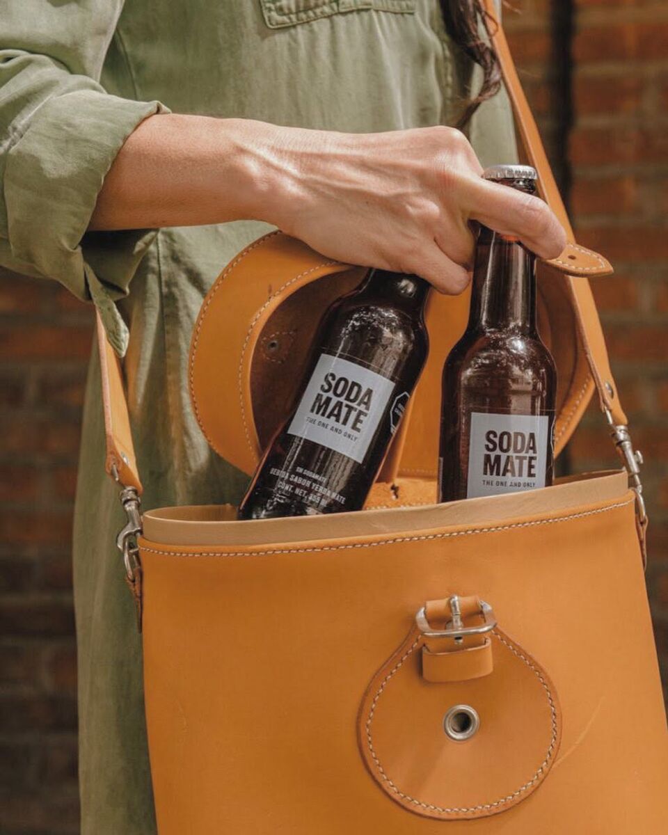 mujer guardando dos botellas de soda mate en una bolsa de cuero