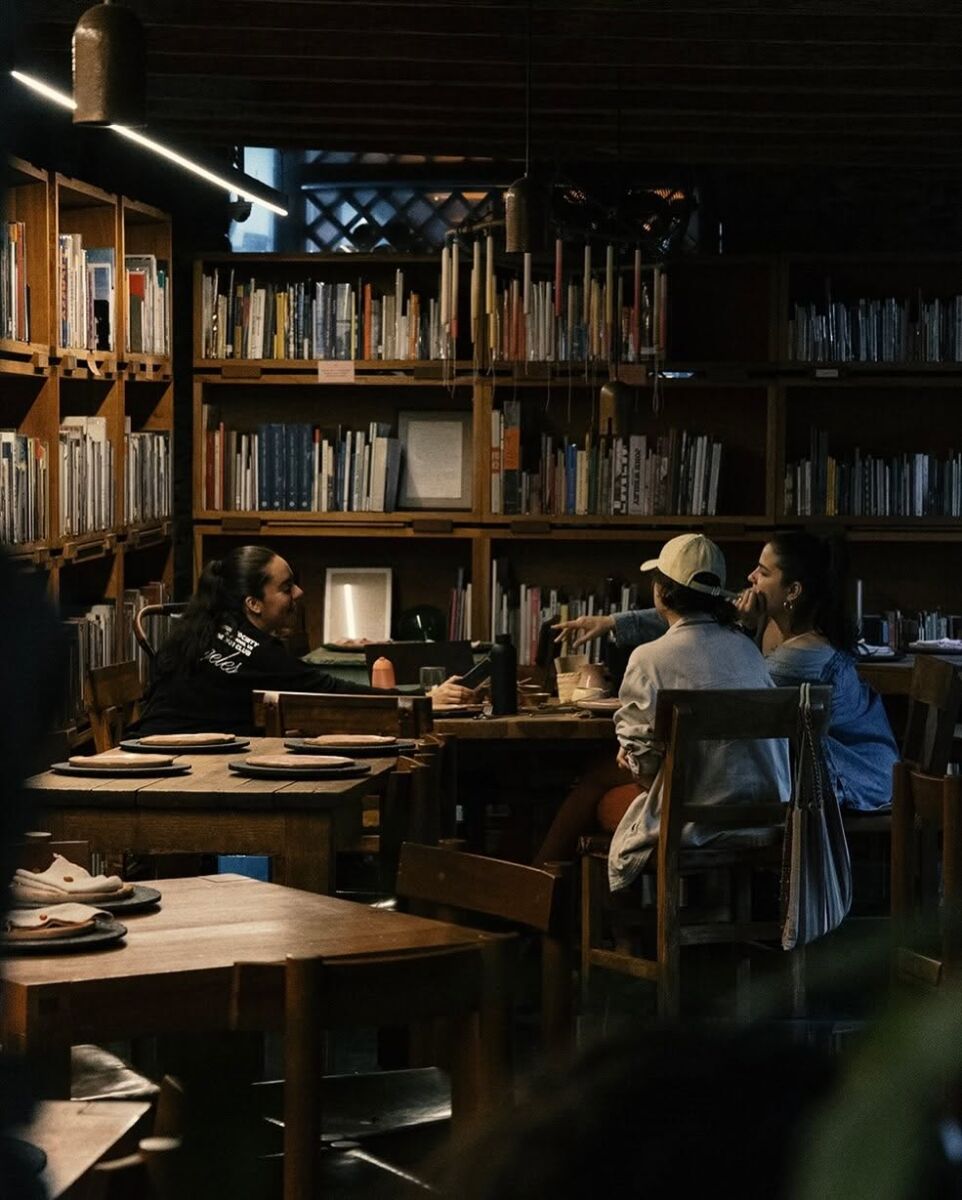 restaurante con luces tenues, mesas de madera y libreros de piso a techo