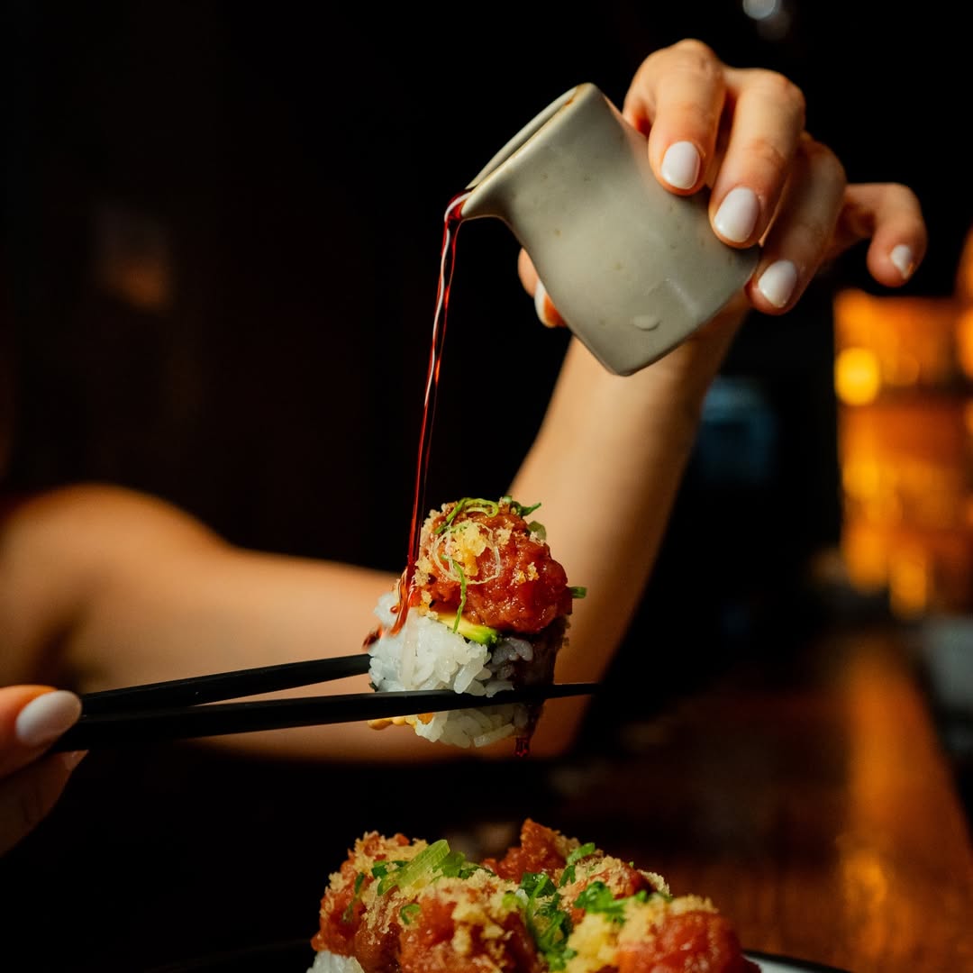 persona poniendo un poco de soya a un rollo de sushi 