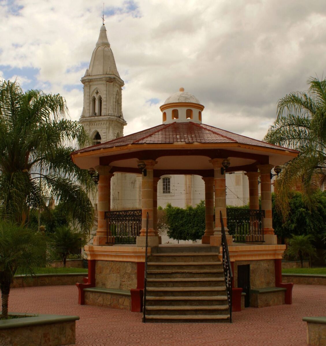 kiosco de apulco, jalisco con palmeras y la torre de una igesia en el fondo