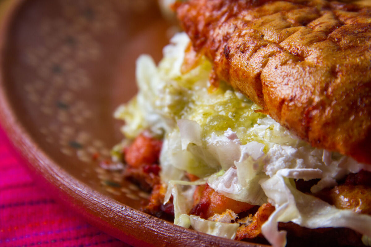 un bolillo en salsa relleno con chorizo y papa, crema, queso y lechuga 