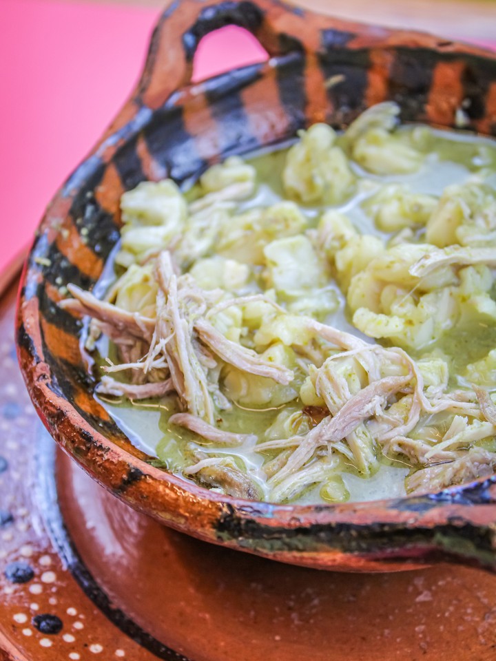 pozol verde con carne de cerdo en fondo rosa