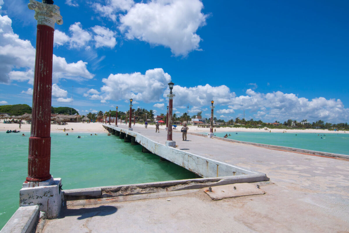 uelle de Sisal con columnas rojas, aguas turquesa cristalinas, playa de arena blanca y bañistas, Pueblo Mágico Yucatán