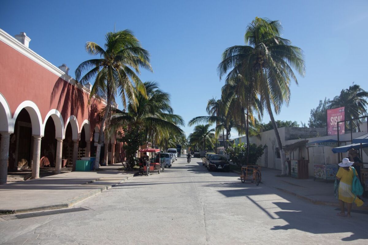 Calle principal de Sisal con casas coloniales rosadas, arcos de cantera, palmeras de coco y triciclos locales, Pueblo Mágico Yucatán