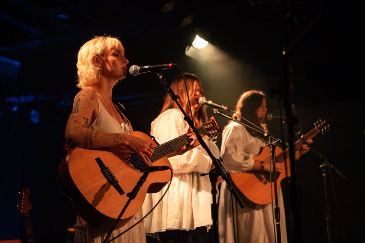 tres mujeres cantando con guitarras acústicas