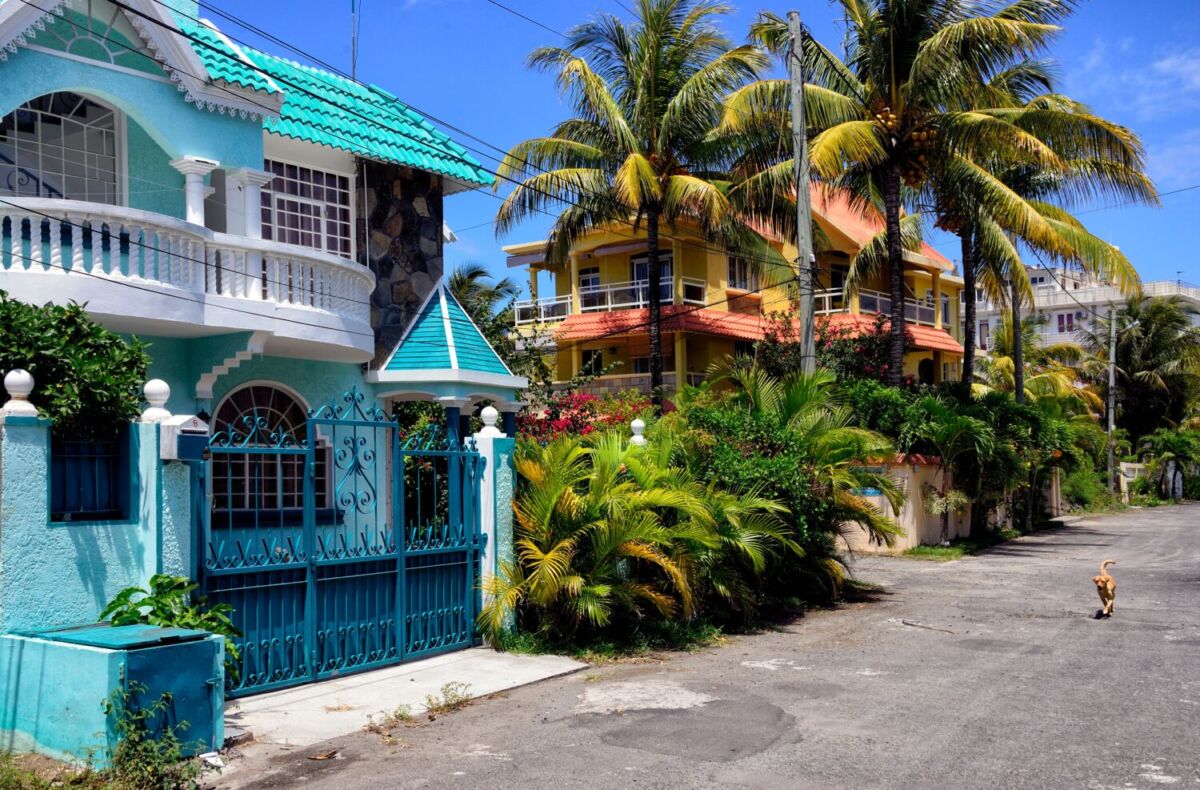 Calle residencial de Mauricio con casas en tonos turquesa y amarillo entre palmeras de coco