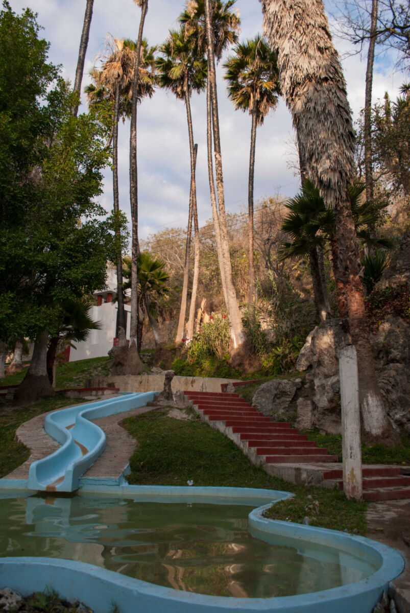 Toboganes azules y albercas de aguas termales sulfuradas rodeados de palmeras en el Balneario Municipal de Tonatico