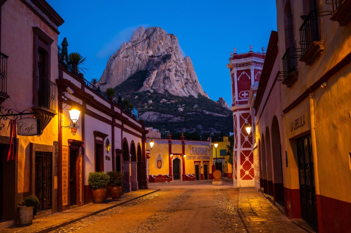Calle empedrada iluminada de noche con la Peña de Bernal alumbrada al fondo, Querétaro