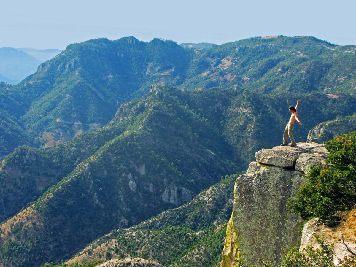 Hombre con los brazos abiertos sobre una roca saliente frente a las montañas de la Sierra Tarahumara