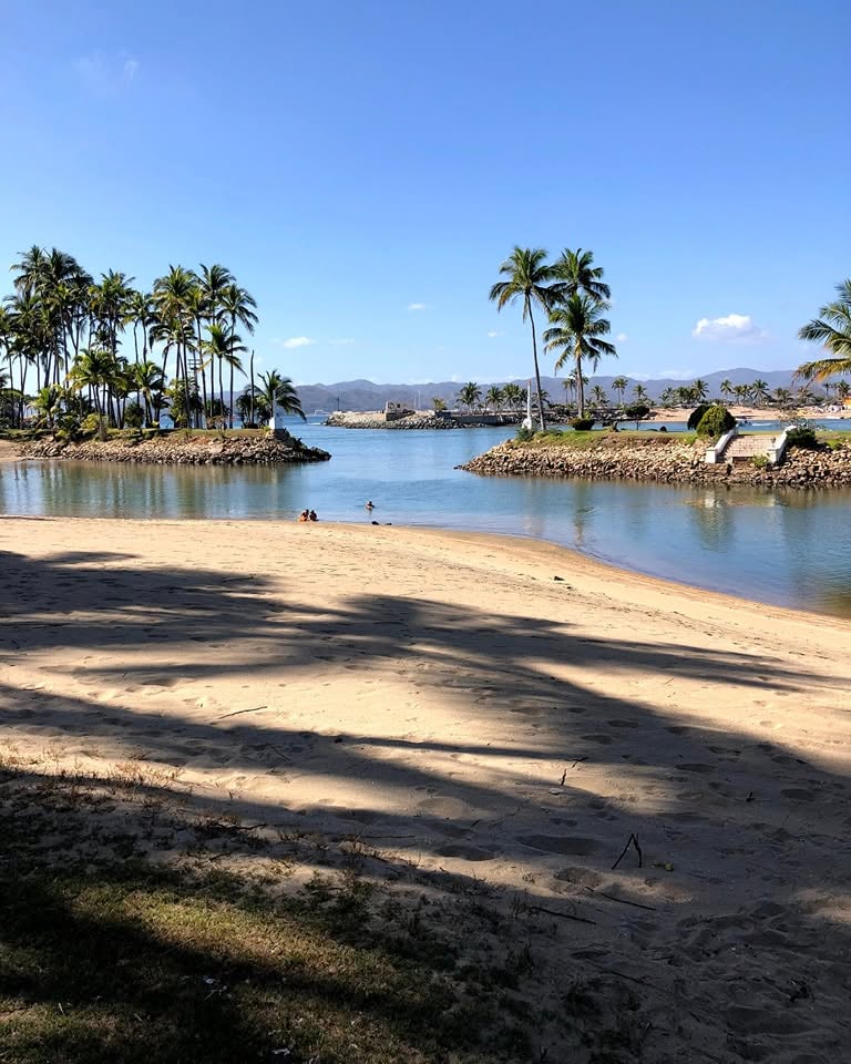 Playa de arena con sombras de palmeras frente al canal de la Laguna de Navidad en la Costa Alegre, Jalisco