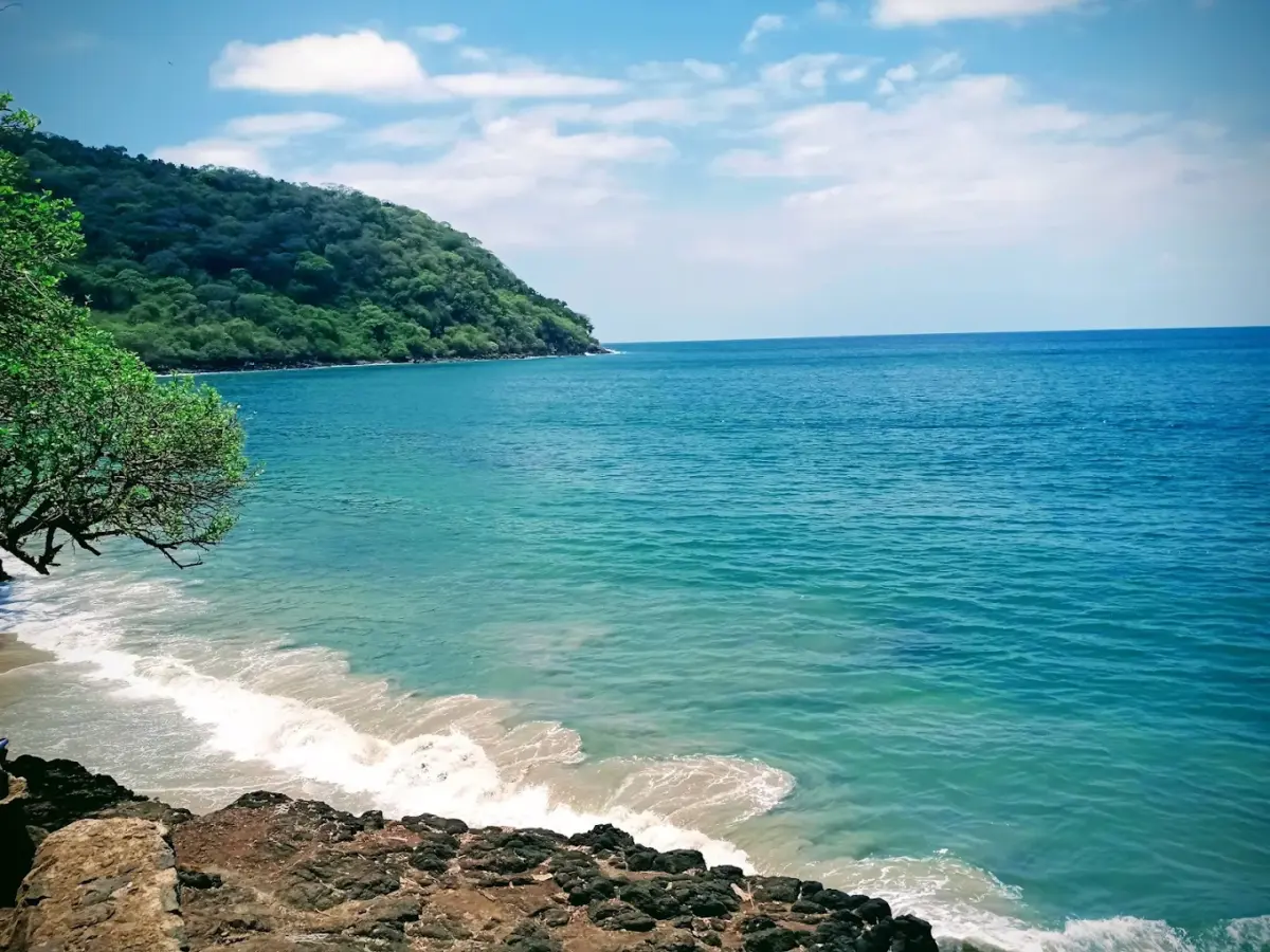 Bañistas en la playa de Los Ayala con el cerro cubierto de vegetación tropical al fondo, Riviera Nayarit