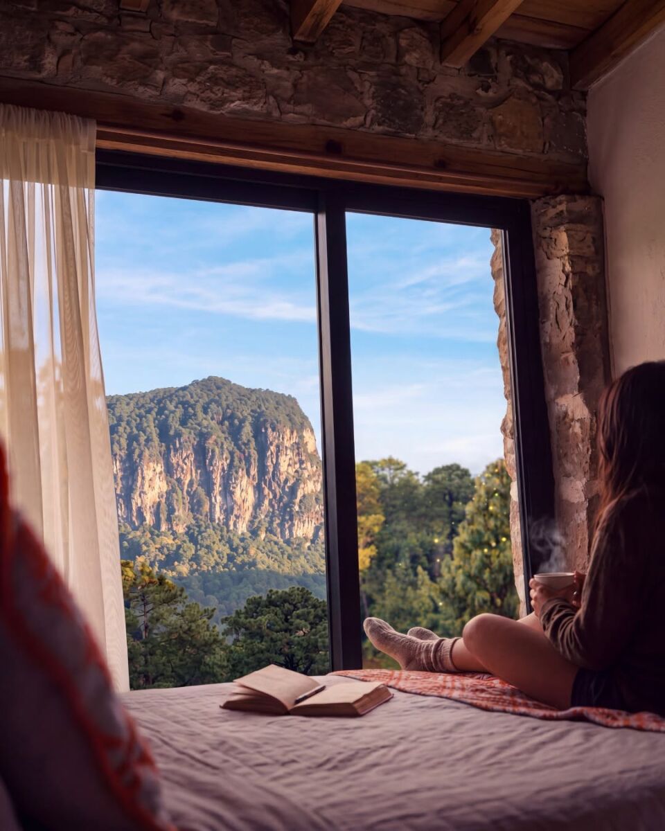 mujer sentada en una cama viendo por la ventana a las montañas