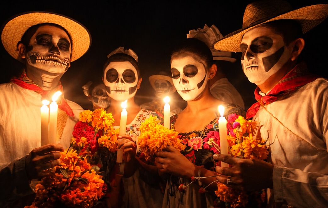 personas intadas de calaca con velas y flores