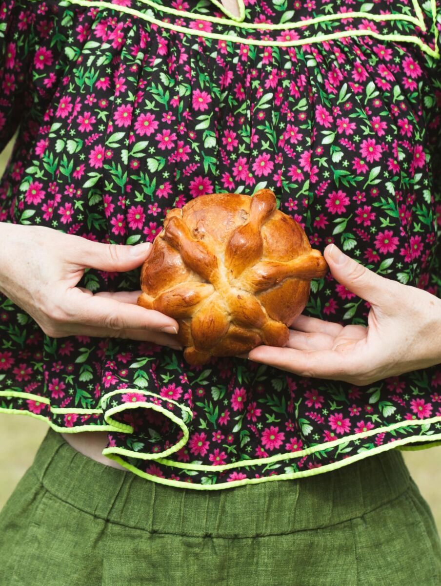mujer con blusa tradicional mexicana mostrando un pan de muerto